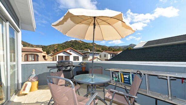 Un balcon équipé d’une table, de chaises, d’un parasol et d’un barbecue.