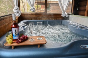 Un bain à remous avec une bouteille de vin Duplin, deux verres et un plateau en bois garni de raisins.