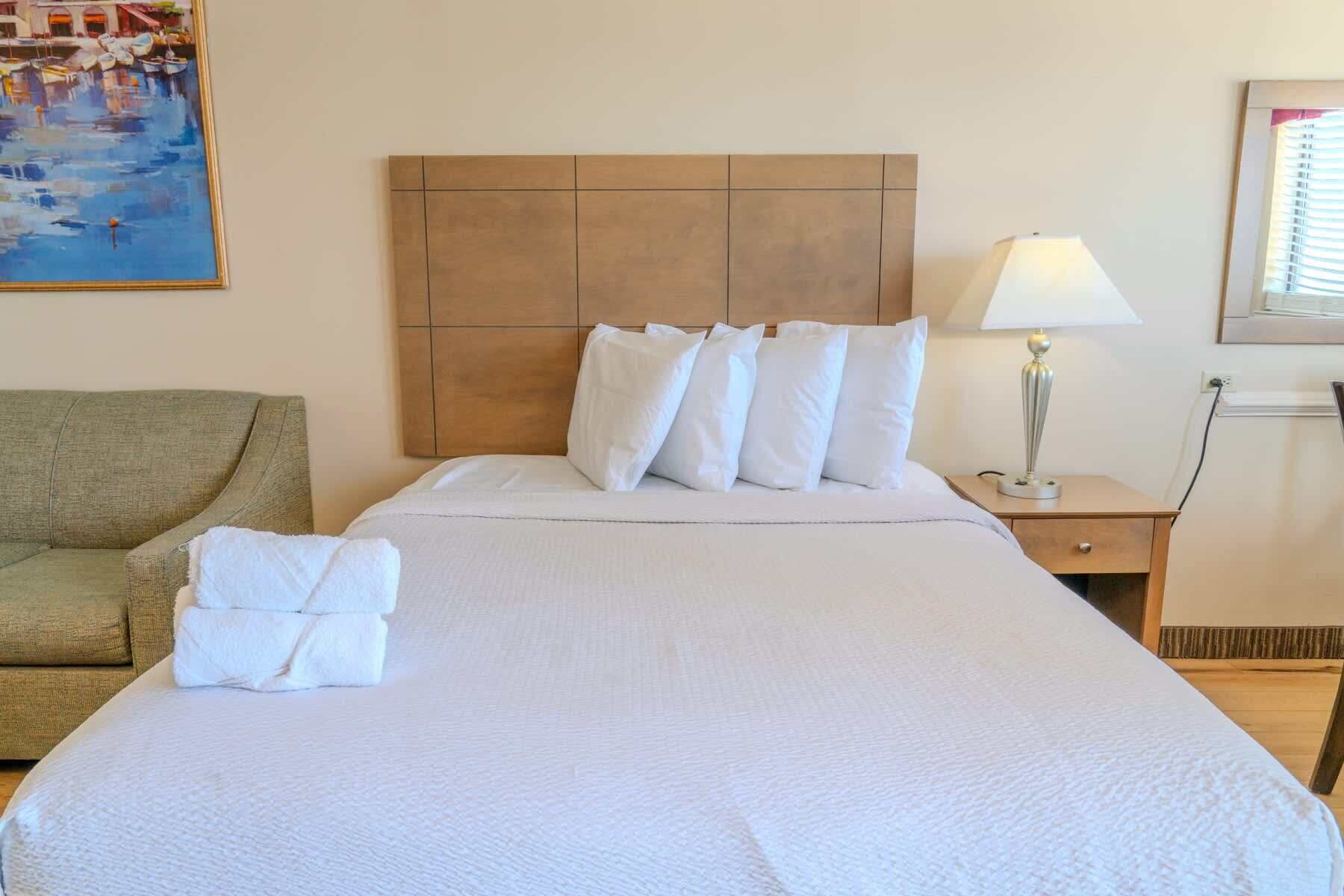 A neatly made bed with white linens, a wooden headboard, and a bedside lamp.
