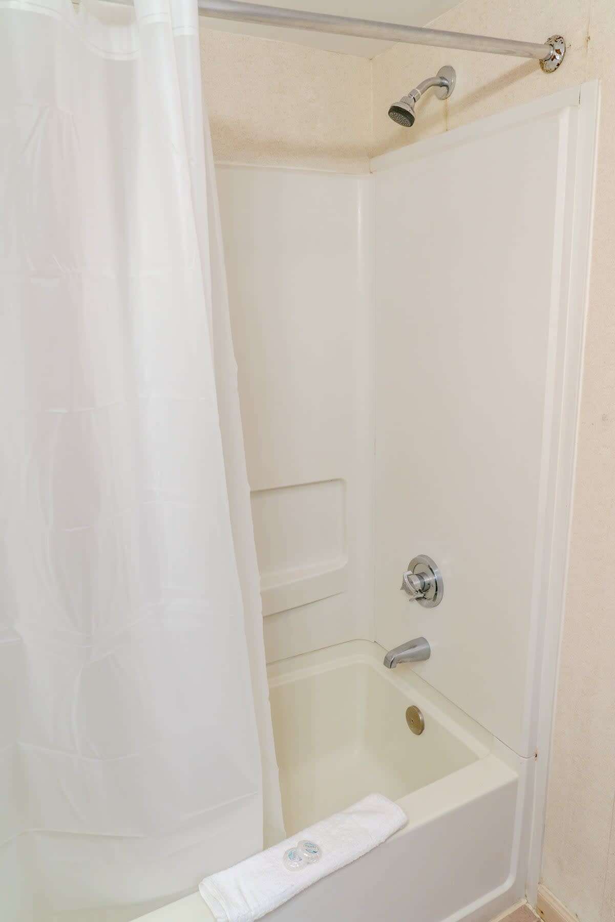 A white shower enclosure with a glass door, a handheld showerhead, and a white towel on the floor.