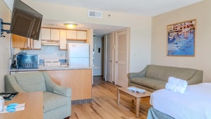A compact hotel room with a kitchenette, a sofa, a bed, and a painting on the wall. - The Four Oh One | Palace (Myrtle Beach)