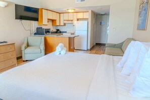 Habitación de hotel con cama, una silla, escritorio con computadora, refrigerador y microondas.