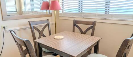 A dining area with a wooden table and chairs, a mirror, and a window with blinds.