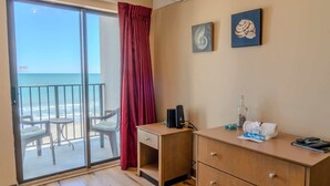 A room with a sliding glass door to a balcony, a desk, a chair, and two wall-mounted paintings. - The Four Oh One | Palace (Myrtle Beach)