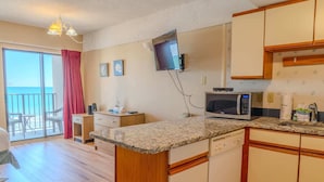 A compact kitchen with a microwave, wooden cabinets, and a small dining area with a table and chairs. - The Four Oh One | Palace (Myrtle Beach)