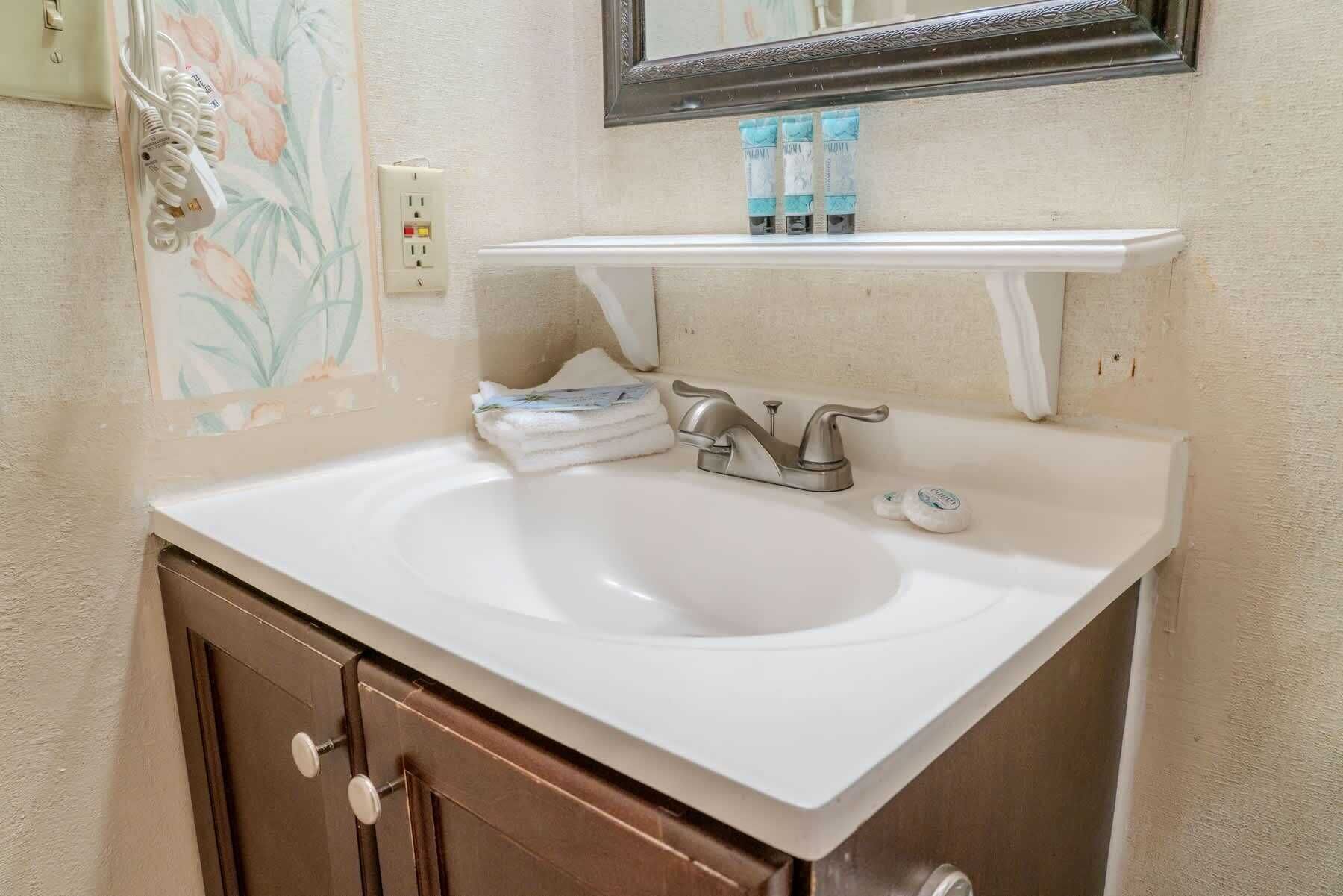 A bathroom with a white sink, a mirror above it, and a towel rack with toiletries.