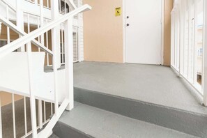 Eine Treppe mit weißen Geländern führt zu einer beigen Tür mit einem Warnschild.