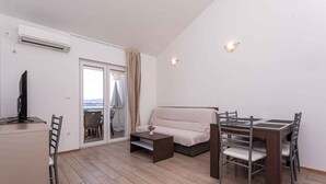Una sala de estar moderna con un sofá, una mesa de comedor con sillas, un televisor sobre un mueble bajo y un ventanal corredizo que da a un balcón.