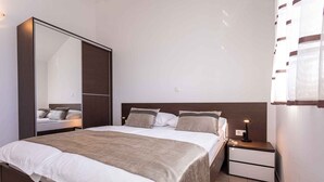 Un dormitorio moderno con una cama grande, un armario, una mesita de noche con lámpara y un espejo.