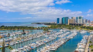 Un puerto deportivo con numerosas embarcaciones amarradas, un horizonte urbano al fondo y un cielo azul despejado.