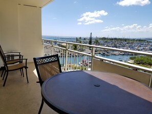 A balcony with a round table and two chairs, overlooking a marina with boats and a clear sky.