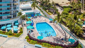A resort with a large swimming pool, lounge areas, and palm trees.