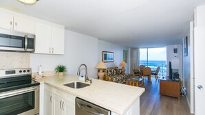A modern kitchen with a built-in microwave, oven, and dishwasher. There is a dining area with a table and chairs, and a view of the ocean through large windows. - Breathtaking 180-Degree Ocean Views, Ilikai Marina, Full Kitchen! (Honolulu)