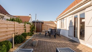 A patio area with a table and chairs, a wooden fence, and a building with a tiled roof. - Vissershuisje 9/18 with parking by Interhome (Bredene)