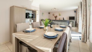 A modern dining area with a long table set for four, a microwave above the table, and a television in the background. - Vissershuisje 9/18 with parking by Interhome (Bredene)