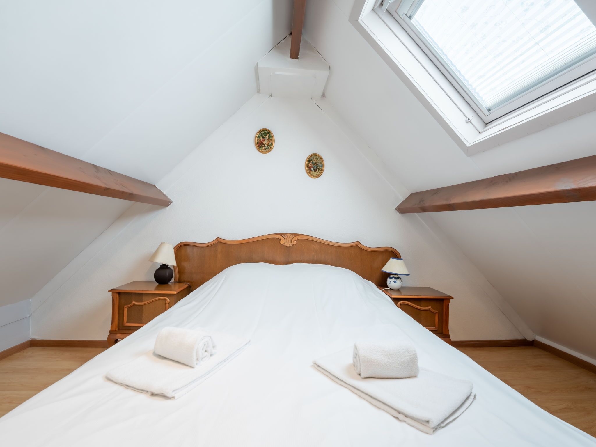 A bedroom with a wooden bed, two nightstands, a window, and a sloped ceiling.