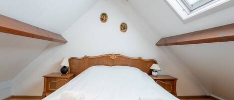 A bedroom with a wooden bed, two nightstands, a window, and a sloped ceiling.