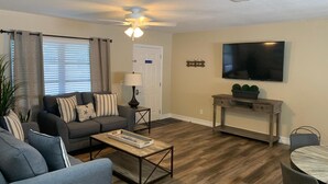 Un salon avec un canapé, une table basse, un téléviseur et un ventilateur de plafond.