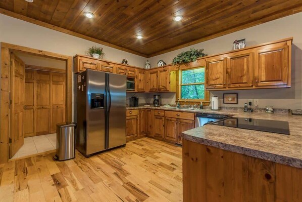 A kitchen with wooden cabinets, a stainless steel refrigerator, a sink, and a window with a view of trees. - THE MOUNTAIN LAUREL |GORGEOUS MOUNTAIN VIEWS (Hiawassee)