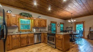 A wooden kitchen with a central island, stainless steel appliances, and a dining area with chairs. - THE MOUNTAIN LAUREL |GORGEOUS MOUNTAIN VIEWS (Hiawassee)