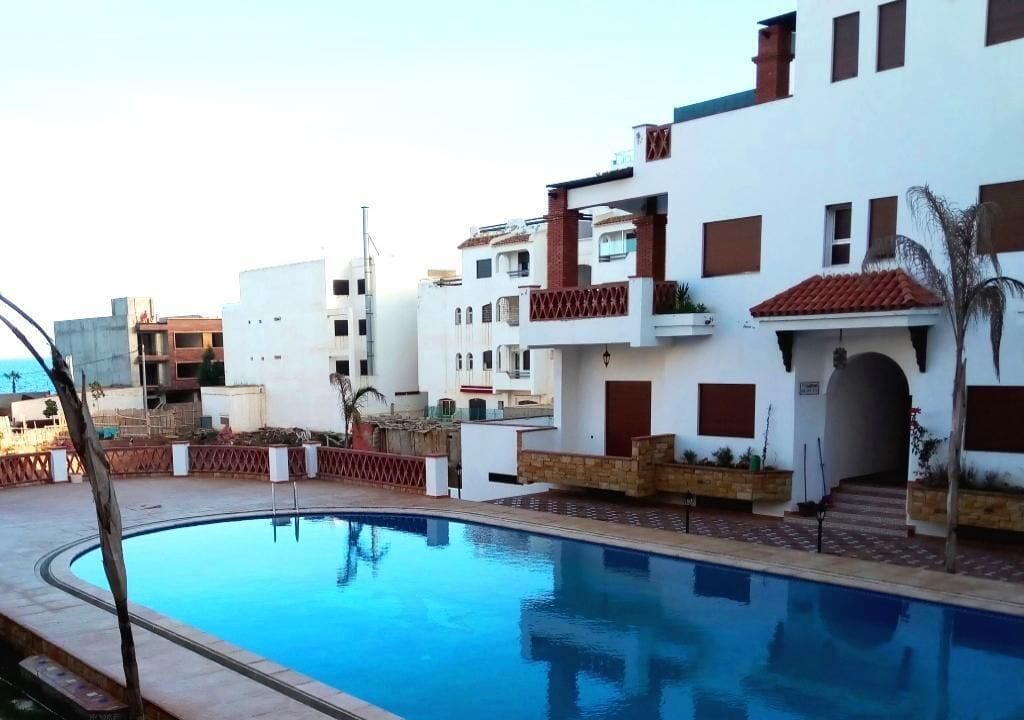 A swimming pool surrounded by modern buildings with balconies and a clear sky.