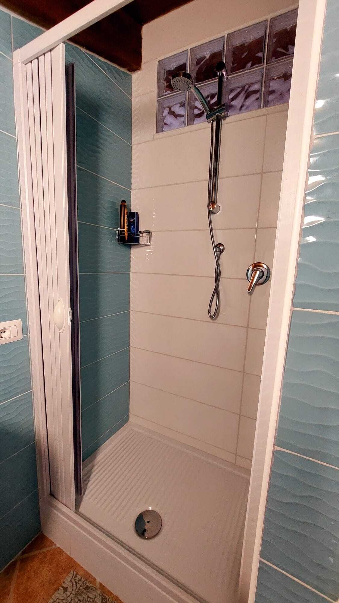 A walk-in shower with a glass door, tiled walls, and a handheld showerhead.