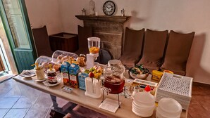 A breakfast table set with various food items and condiments, a coffee maker, and a fruit bowl.