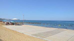 Une plage avec une promenade en bois, des parasols, et des gens qui se baignent et prennent des bains de soleil.