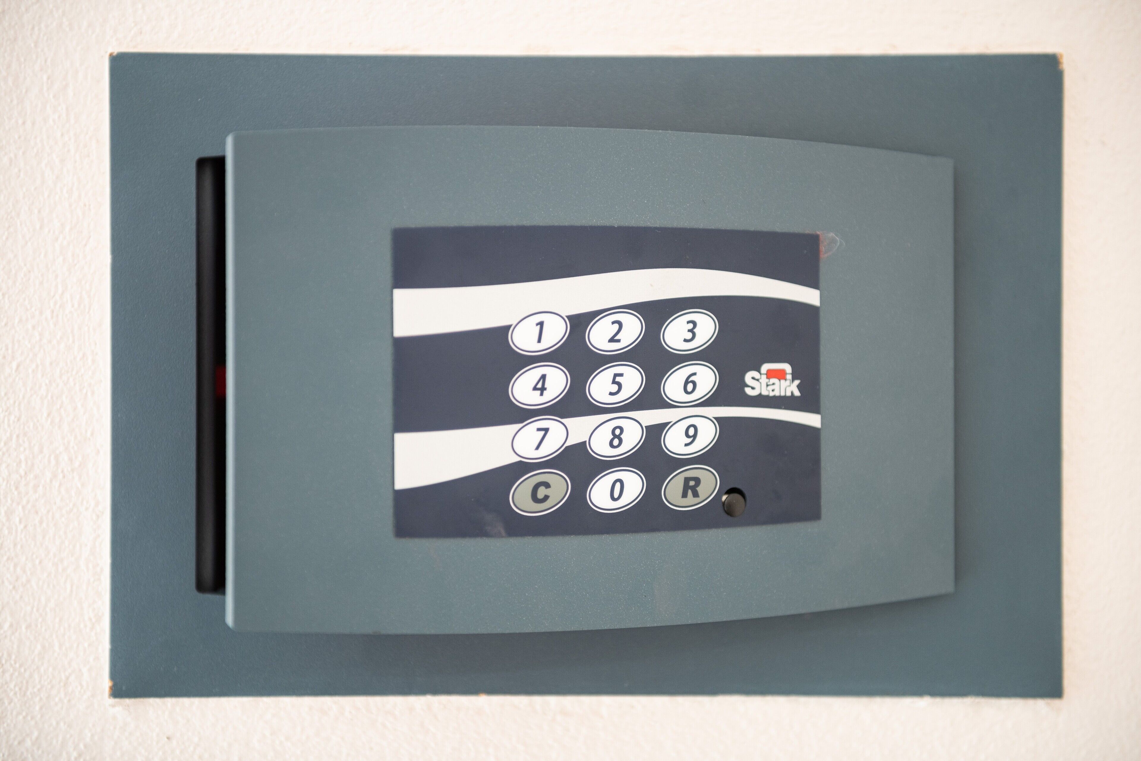 Un panel de control de seguridad fijado a la pared, con teclado numérico y un botón rojo que dice 'Talk'.