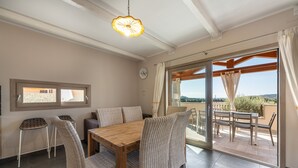 A dining area with a wooden table and wicker chairs, a ceiling light fixture, and a view through a glass door to an outdoor patio. - Luxurious Holiday Home with Pool, Terrace, Wi-Fi & Air Conditioning; Parking Available, Smaller Pets Allowed (domus de maria)