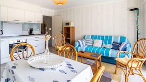 Ein modernes, helles Wohnzimmer mit einem blau gestreiften Sofa, Holzstühlen und einem Esstisch mit weißem Tischleinen.