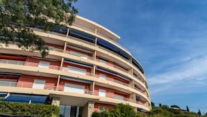 Ein mehrstöckiges Hotel mit geschwungener Fassade, Balkonen in jeder Etage und einem Parkplatz davor.