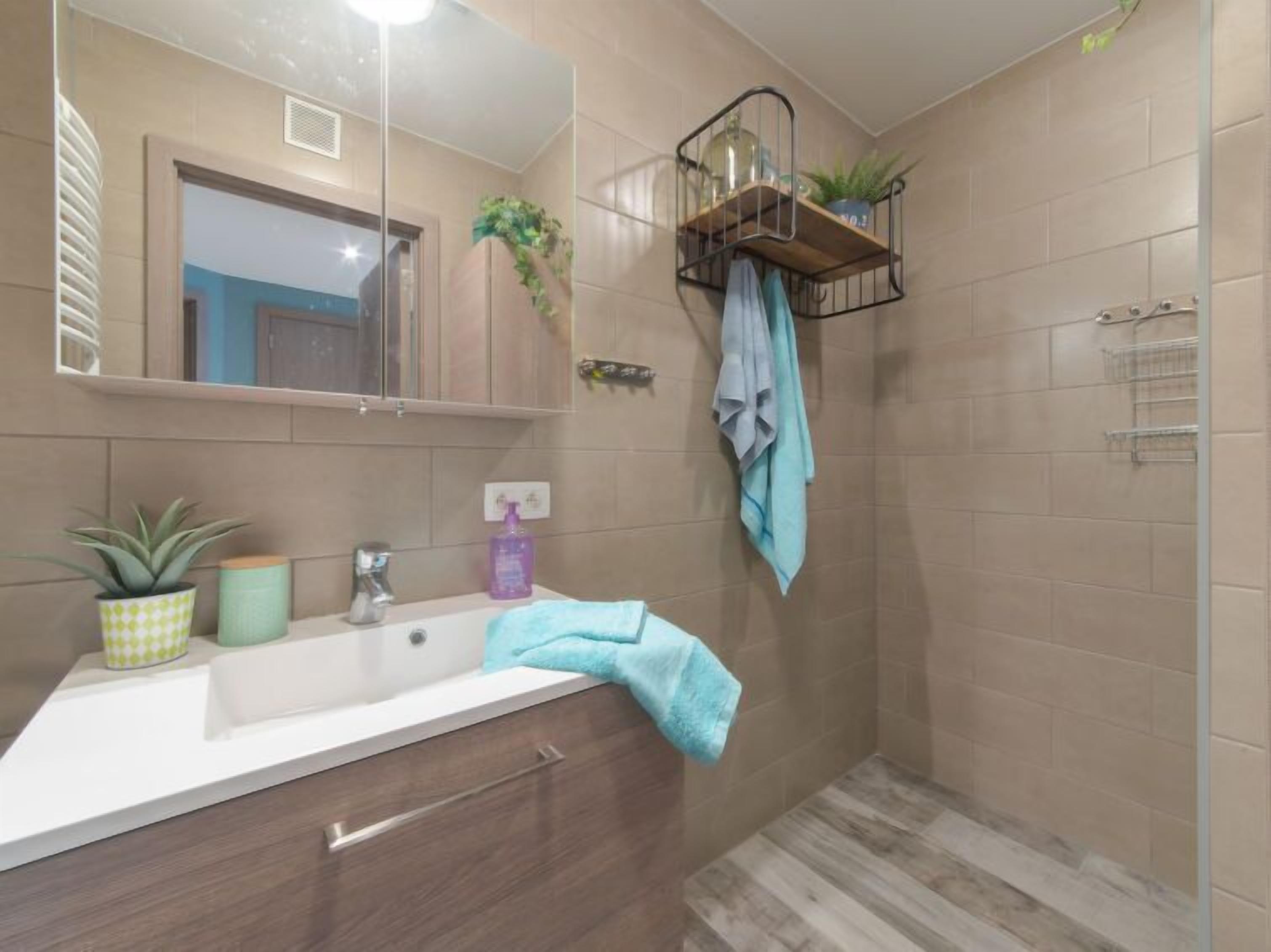 A modern bathroom with a large mirror, a sink, a towel rack, and a shower area.