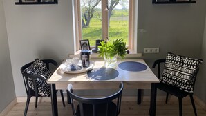 A dining area with a wooden table, black chairs, a vase with green plants, a coffee maker, and framed pictures on shelves. - Newly renovated traditional farmhouse (Ģibuļi)