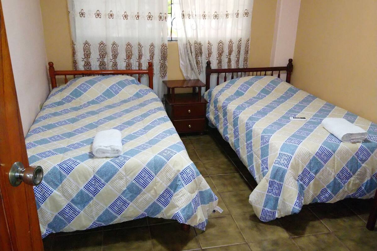 A room with two beds, a wooden door, a small table, and a curtain with a floral pattern.