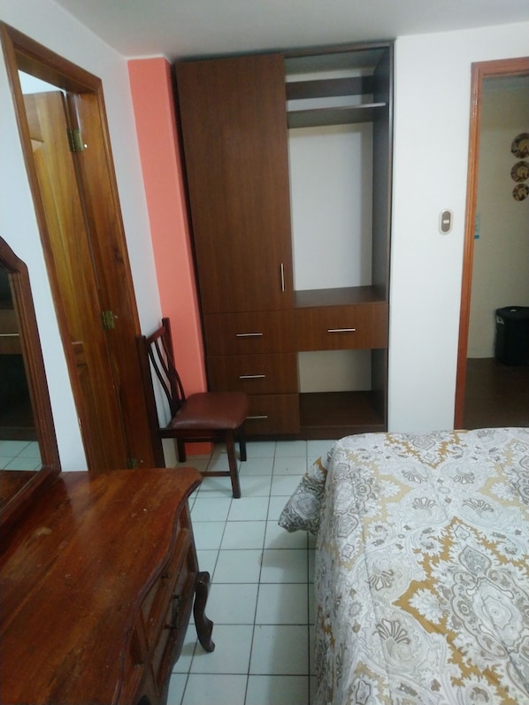A bedroom with a bed, a wooden dresser, a chair, a wardrobe, and a door.