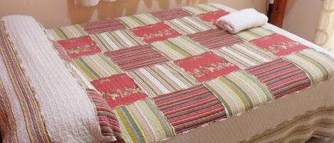 Un letto rifatto con una coperta a righe, un comodino e una ventola da terra.
