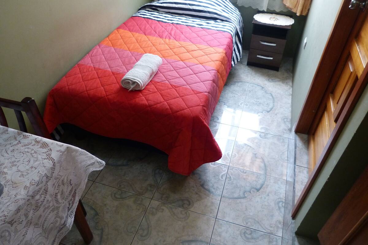 A small, neatly arranged bedroom with a bed, a nightstand, a chair, and a table.