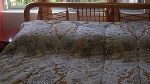 A bed with a patterned bedspread, curtains, and a window with a view of greenery. - Hostal Terito (Puerto Baquerizo Moreno)
