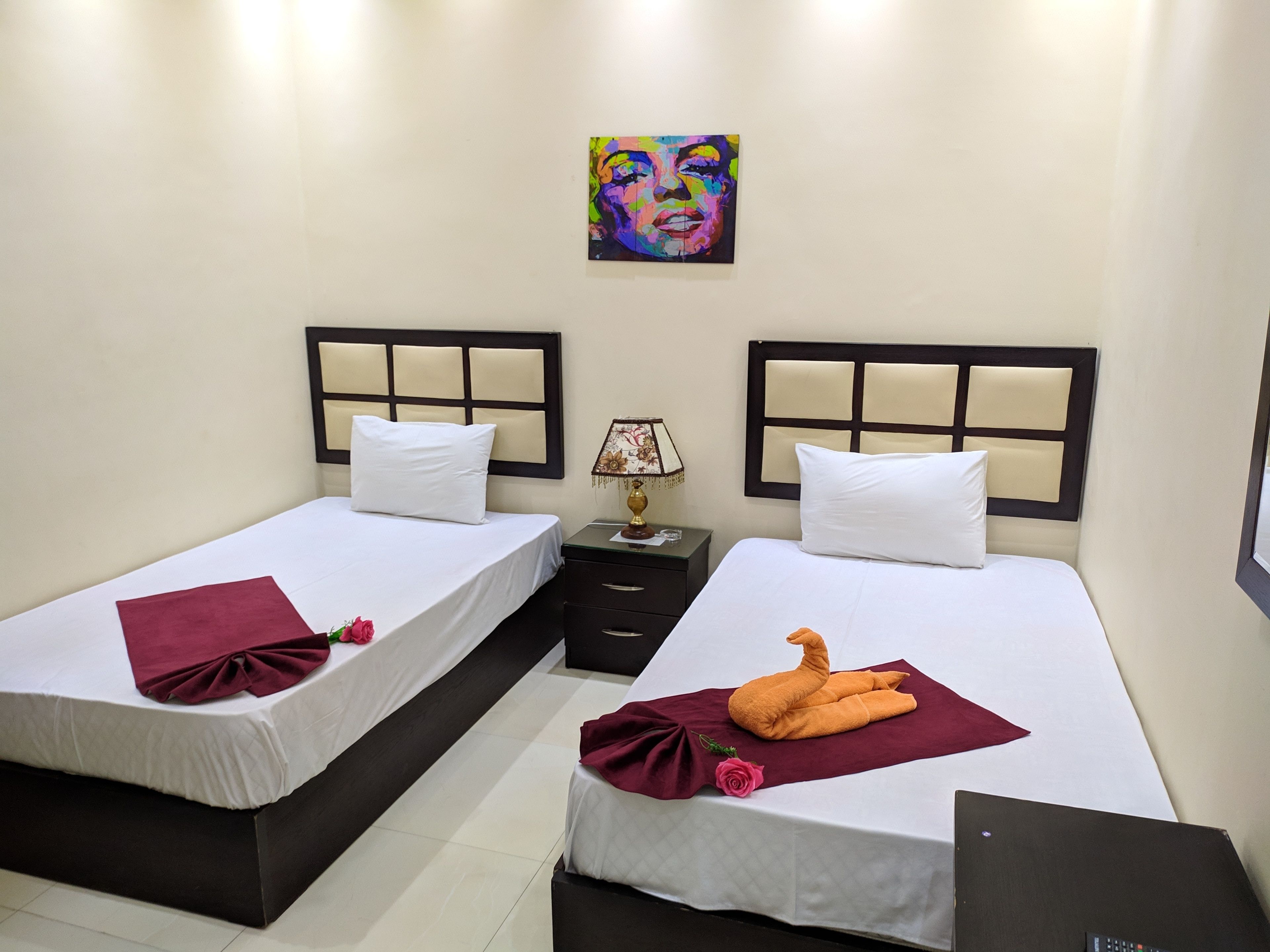Two single beds with headboards, a nightstand with a lamp, and a colorful painting on the wall.