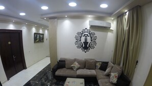 A living room with a sofa, a small table, a decorative wall piece, and an air conditioner. - New City Hotel (Cairo)