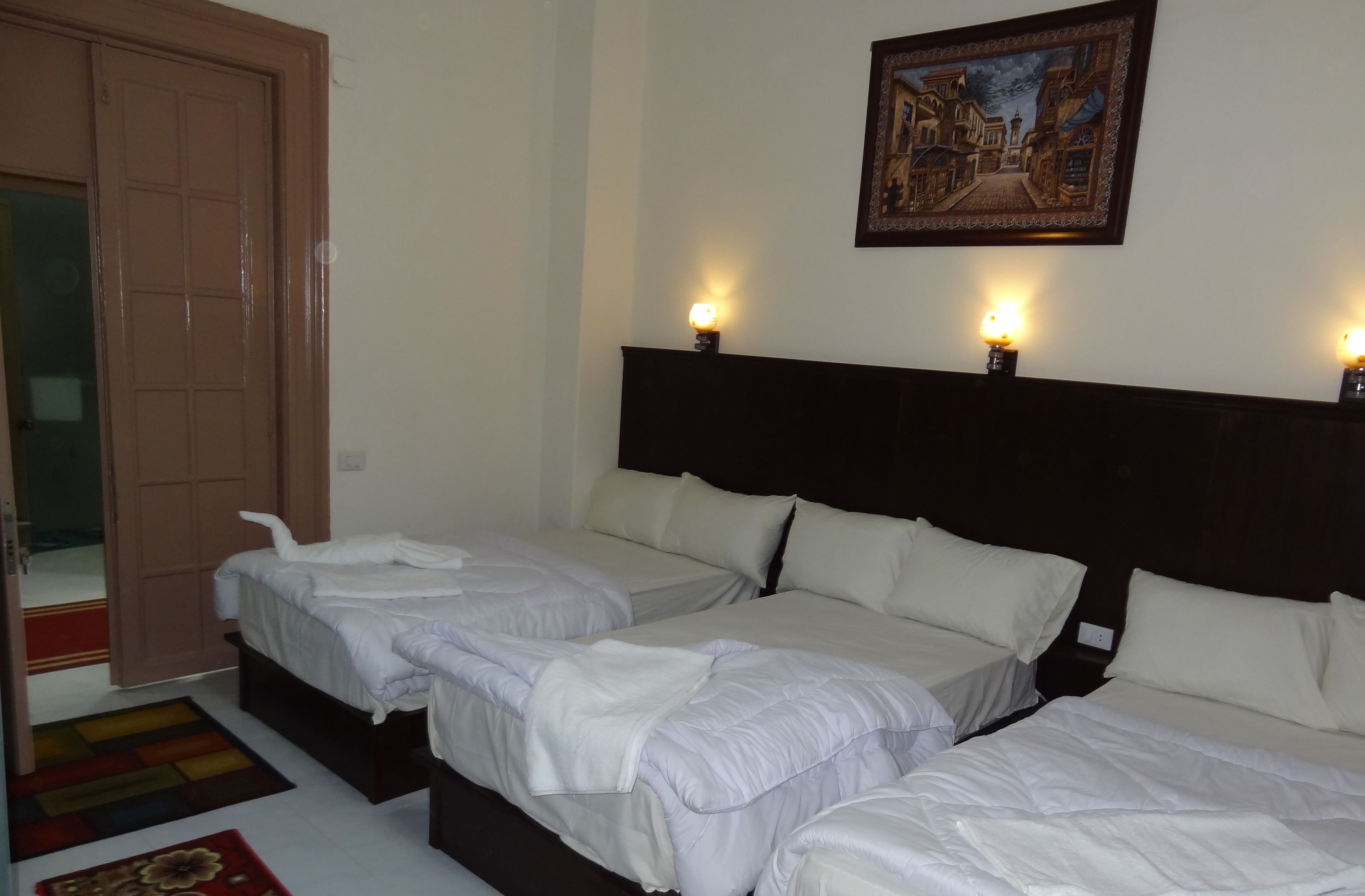 A hotel room with two beds, a wooden headboard, a painting on the wall, and a door with a mirror.