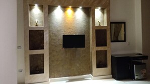 A room with a flat-screen TV mounted on a textured wall, recessed lighting, and a small cabinet with a mirror. - New City Hotel (Cairo)
