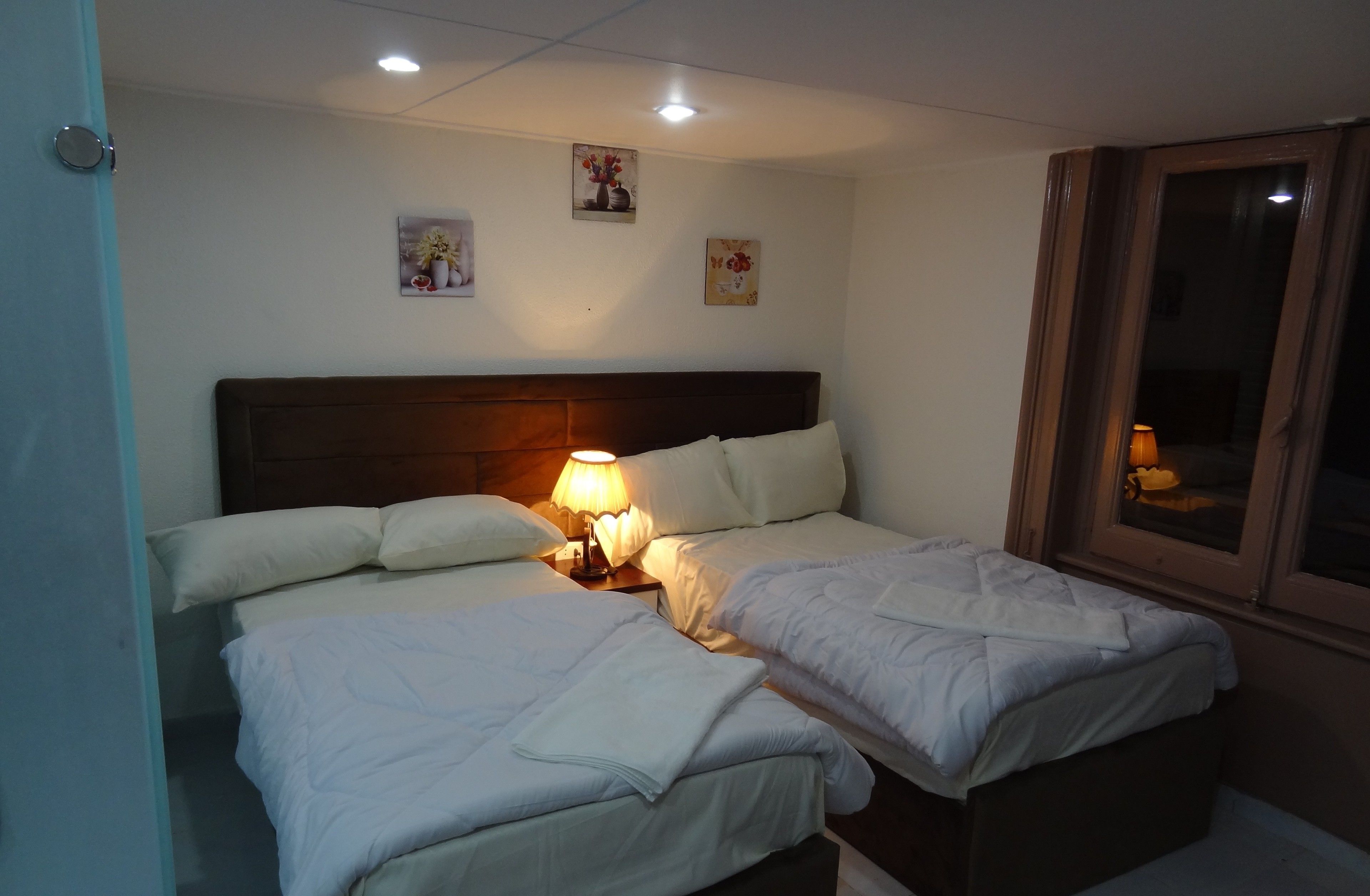 Habitación de hotel con dos camas, cabecero de madera, lámpara de noche y decoración en la pared.