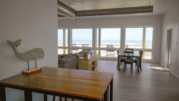 A spacious living area with a wooden table, a sofa, and a dining table with chairs. Large windows provide a view of the beach. - BEACHFRONT on 1 acre lot with incredible beach and bay views.  (Freeport)