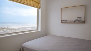 Una habitación con una cama, un ventanal con vista a la playa y un cuadro en la pared.