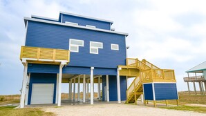 A two-story building with a blue exterior, a covered outdoor area, and a wooden staircase leading to a deck. - BEACHFRONT on 1 acre lot with incredible beach and bay views.  (Freeport)