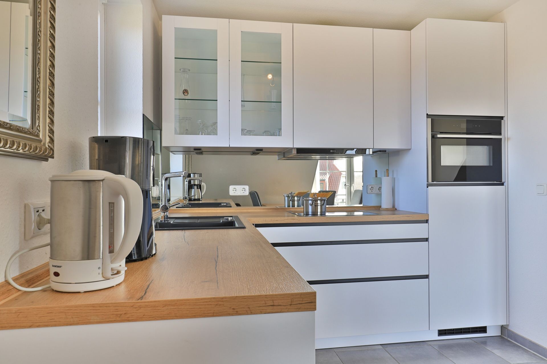 A modern kitchen with white cabinetry, a built-in oven, and a coffee maker.