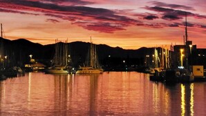 Un puerto deportivo al atardecer con barcos amarrados, cielo despejado y colinas a lo lejos.