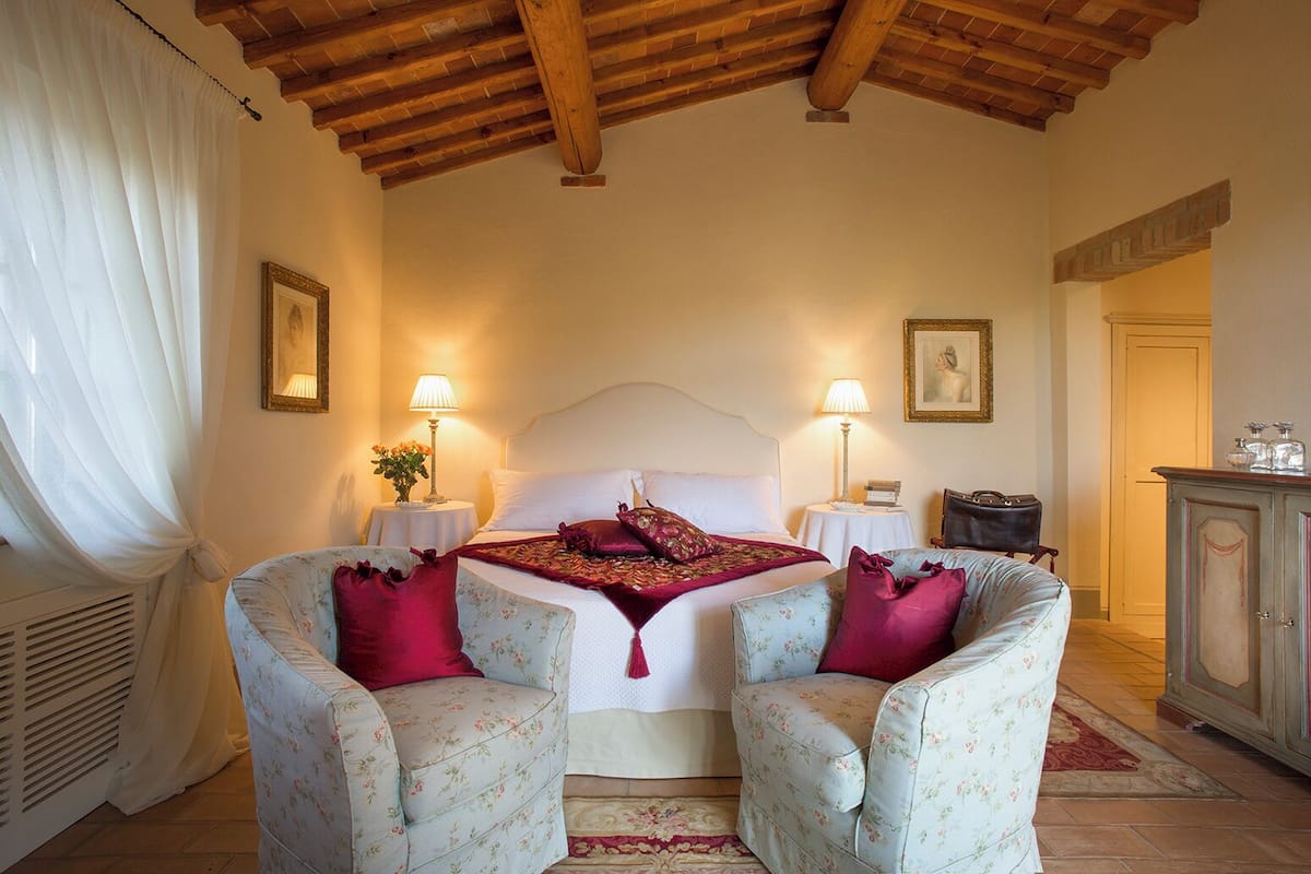 Une chambre à coucher avec un grand lit, deux fauteuils, une table de chevet avec une lampe et une armoire.